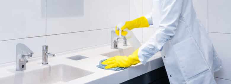 Janitor cleaning sink in public washroom with cloth